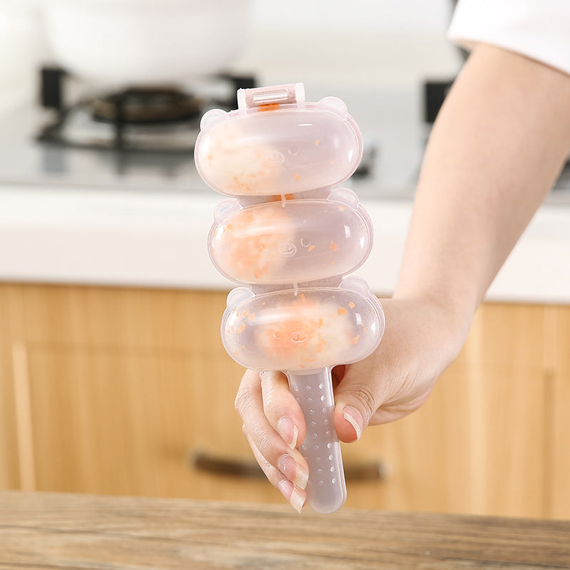 Hand holding a transparent silicone rice ball mold with three compartments filled with pink ice pops in a kitchen setting.