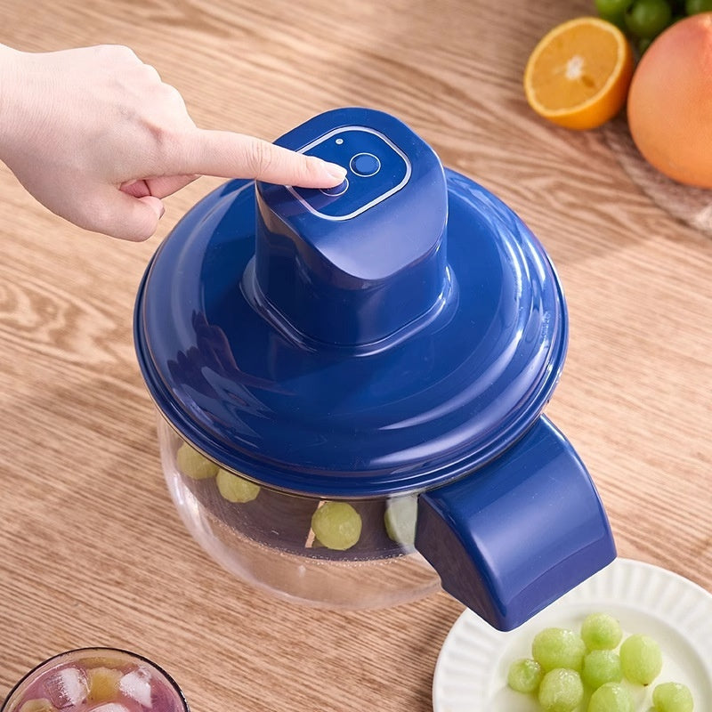 Blue electric fruit and vegetables peeler with a hand pressing down on a wooden table, surrounded by fruits.