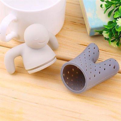 Silicone tea infuser shaped like a person on a wooden surface with a mug and plant in the background.