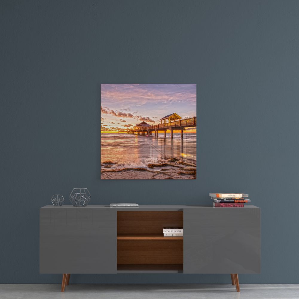 Sunset pier glass wall art on a blue-gray wall above a gray sideboard with wood shelves