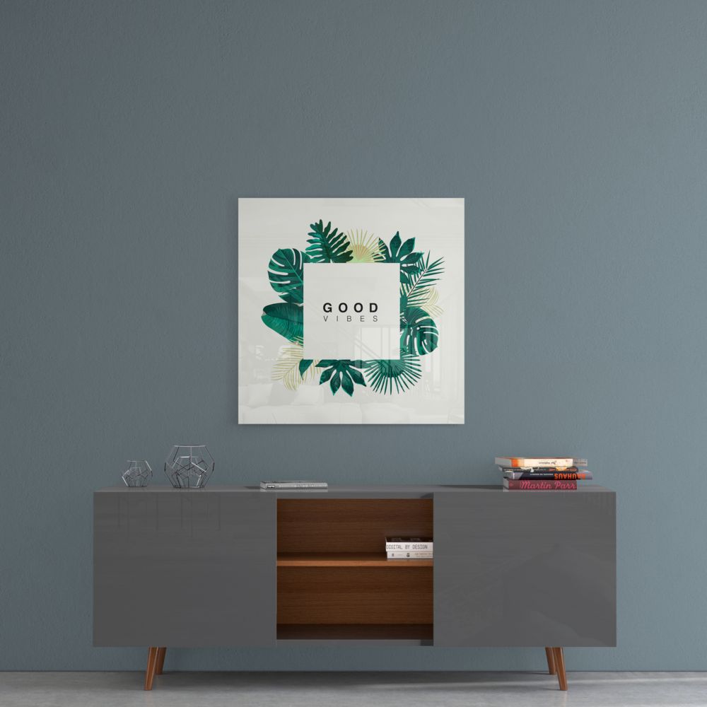 Good Vibes tropical leaves glass wall art above a gray sideboard with a wood shelf on a blue-gray wall