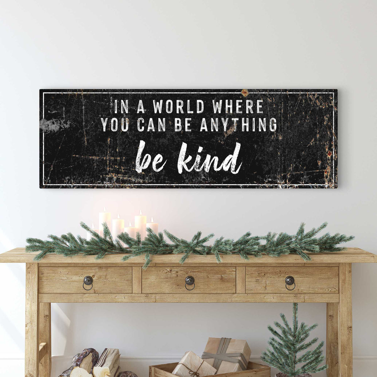 Be Kind canvas sign in the black style with white letters, above a wood console with a pine garland