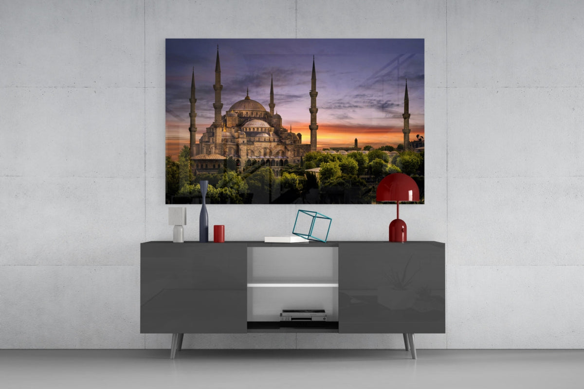 Mosque at purple dusk glass wall art above a gray sideboard with a red table lamp