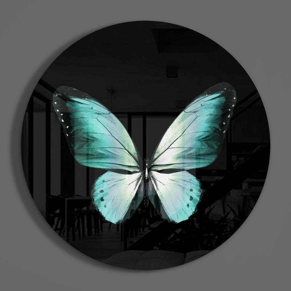 Turquoise butterfly on black round glass wall art hanging on a plain gray wall