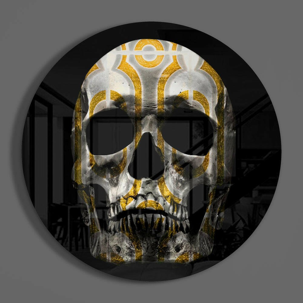 Gold loop pattern skull round glass disc casting a soft shadow on a gray wall
