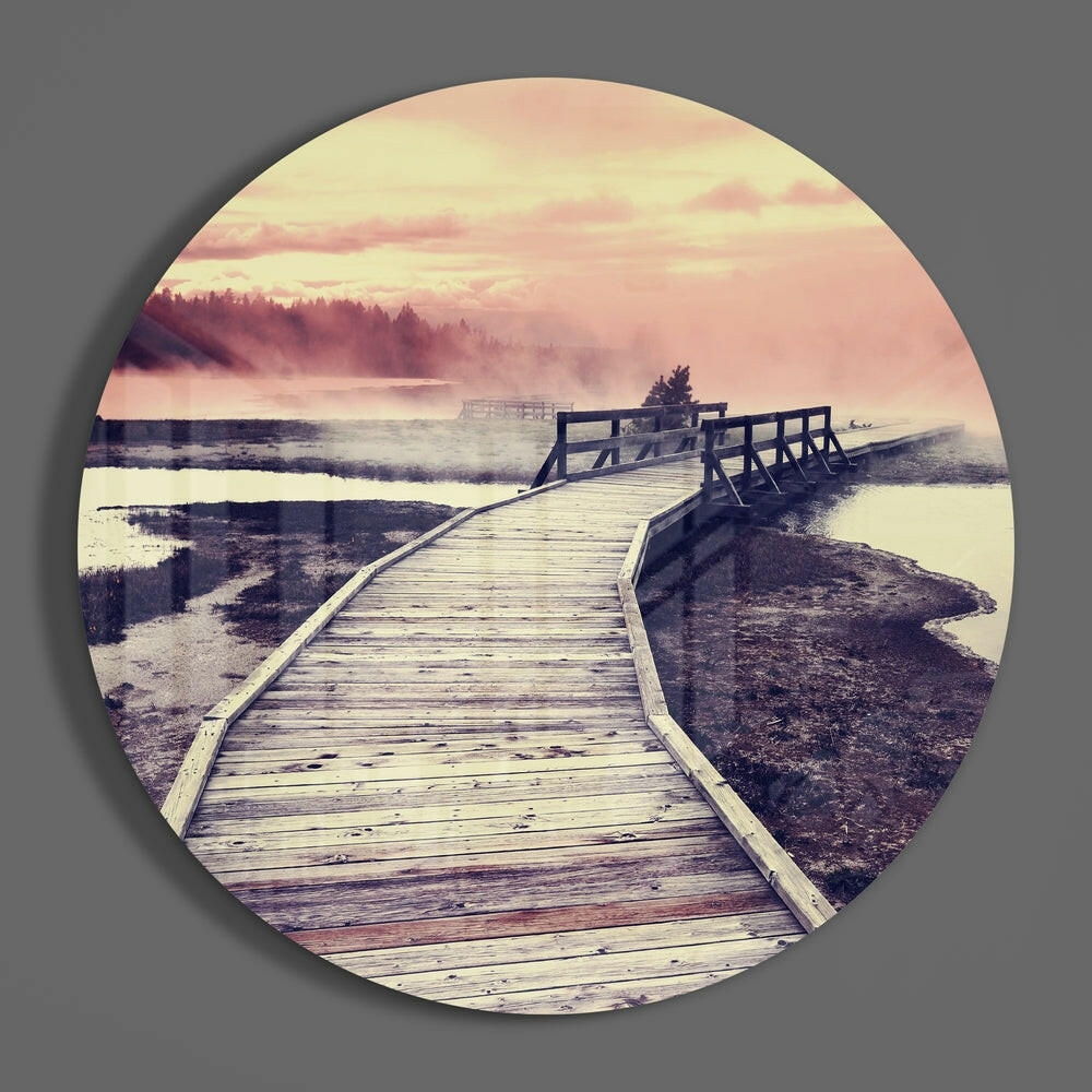 Pink sky wetland boardwalk round glass wall art on a plain gray wall, glossy glass disc seen from the front