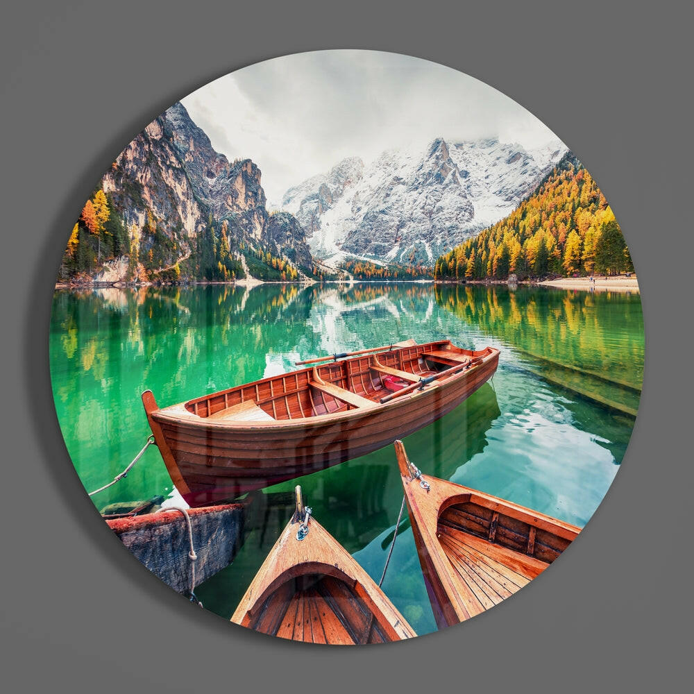 Emerald lake and wooden boats round glass wall art on a gray wall, showing the glossy glass face