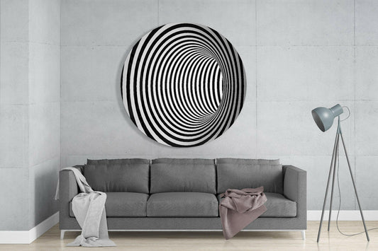 Spiral tunnel illusion round glass wall art above a gray sofa beside a tripod floor lamp on a pale concrete wall