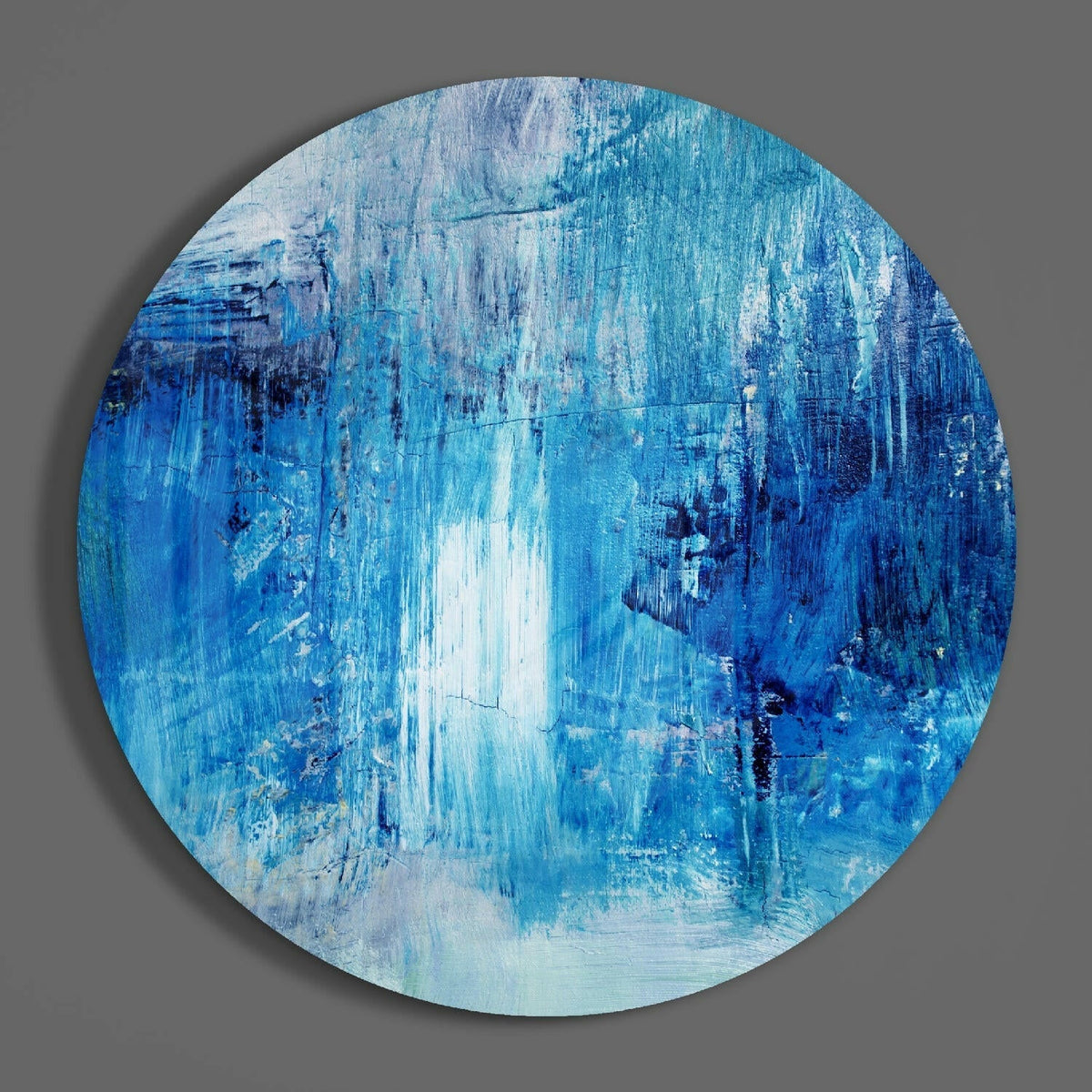 Blue brushstroke round glass wall art hanging on a plain gray wall