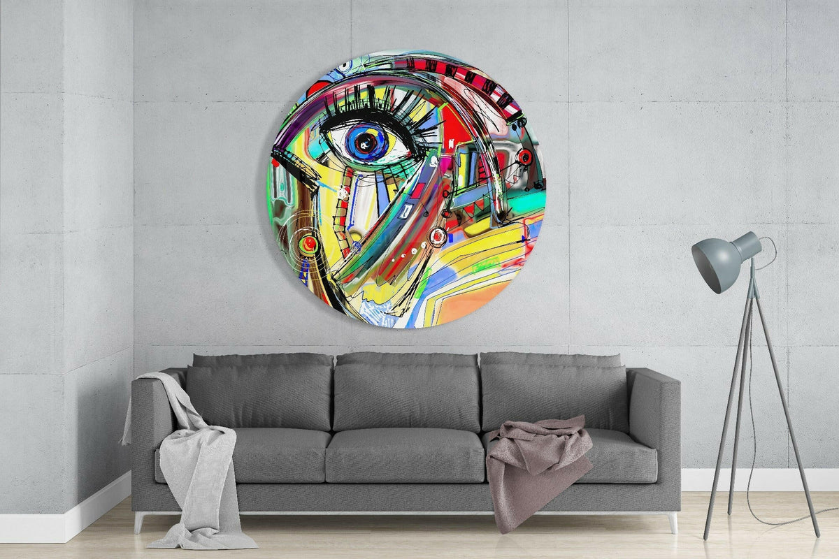 Abstract eye face round glass wall art above a gray sofa with a tripod floor lamp