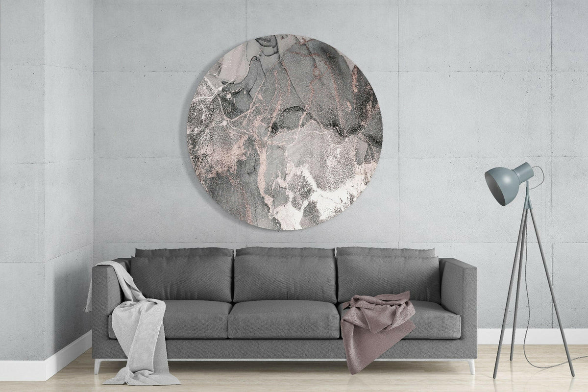 Gray and rose gold marble round glass wall art above a gray sofa beside a tripod floor lamp on a pale concrete wall