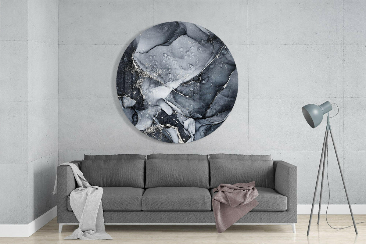 Charcoal silver ink marble round glass wall art above a gray sofa with draped throws on a pale concrete wall
