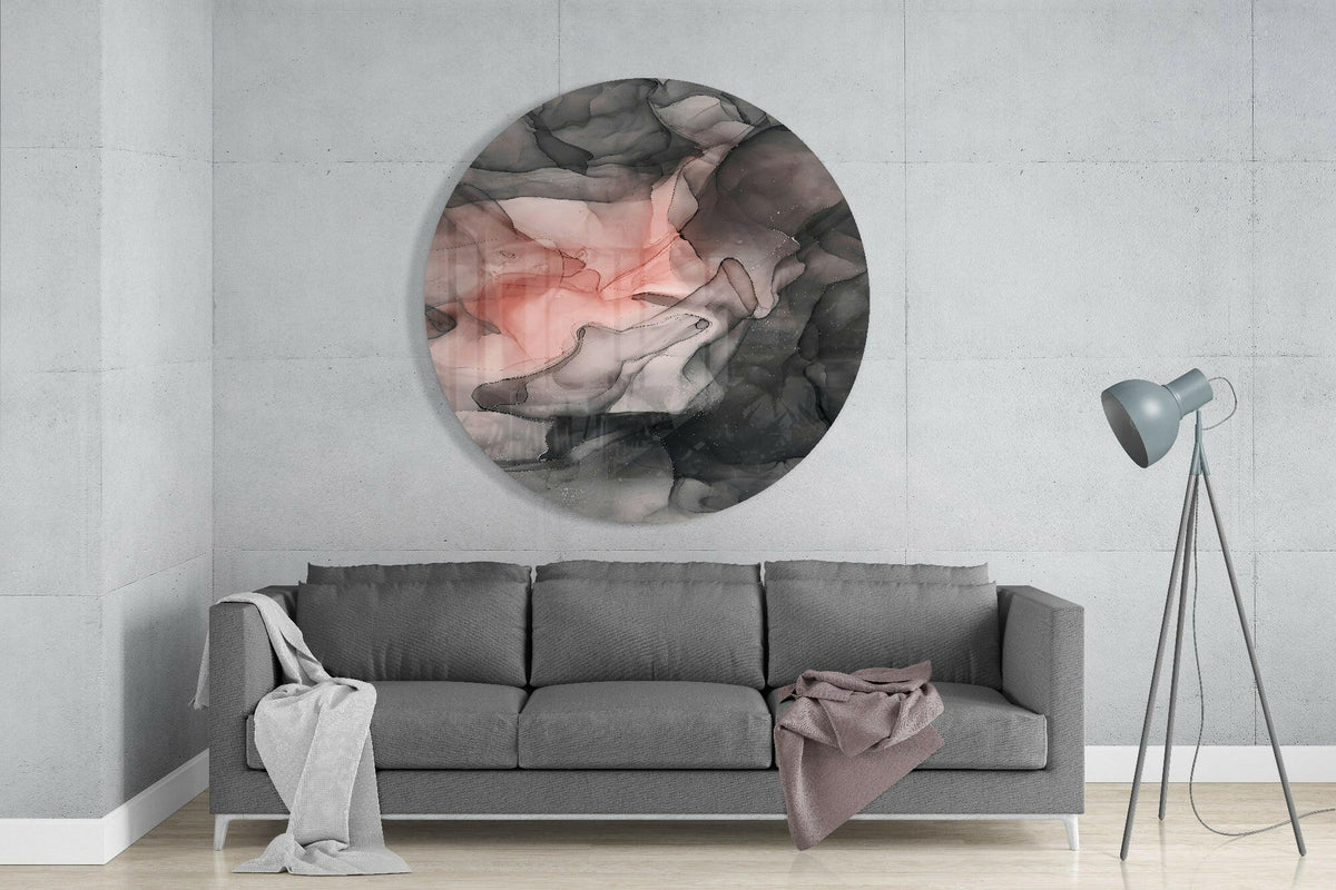 Coral and black ink flow round glass wall art above a gray sofa with draped throws on a pale concrete wall