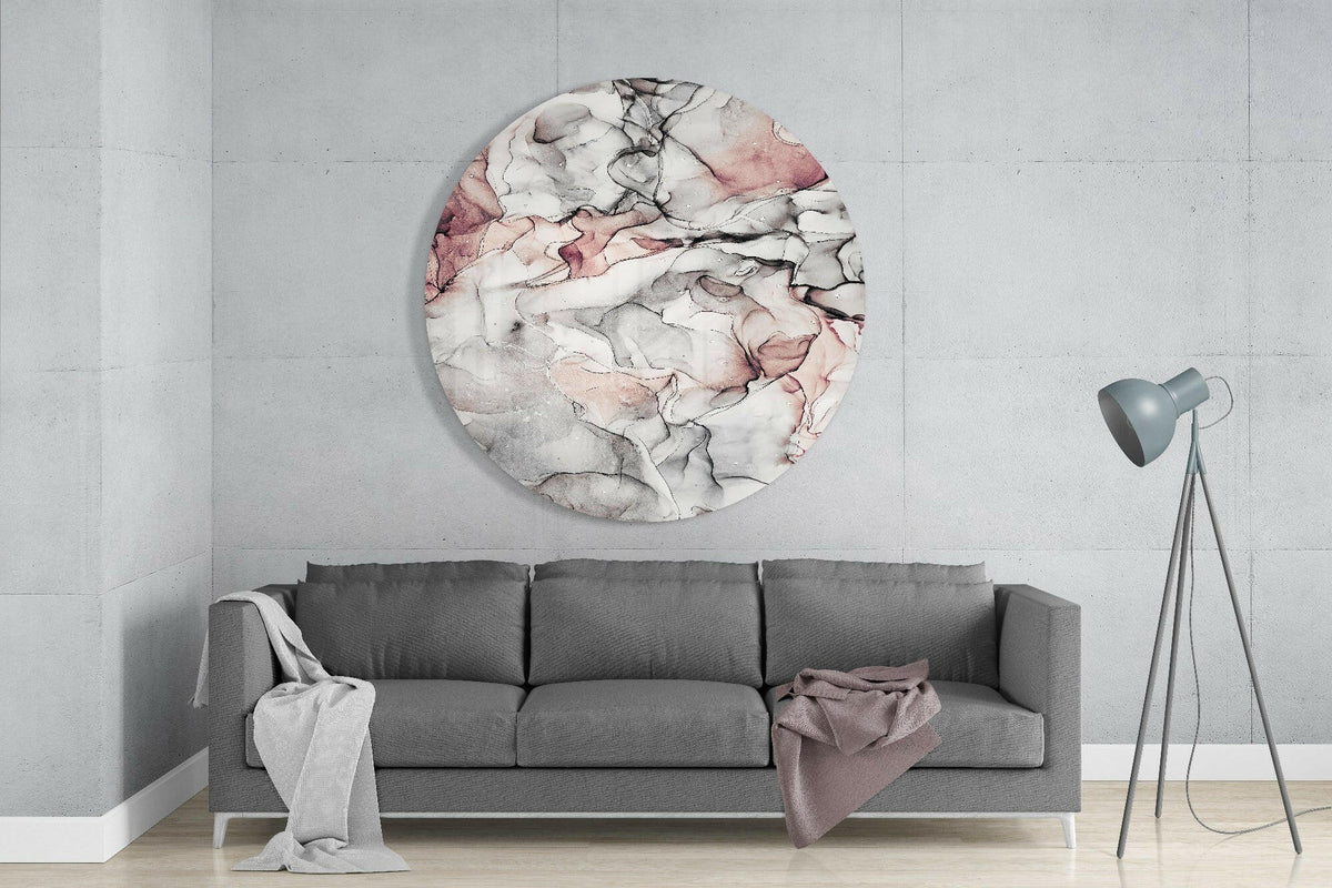Soft blush and gray marble round glass wall art above a gray sofa beside a gray tripod floor lamp on a pale concrete wall