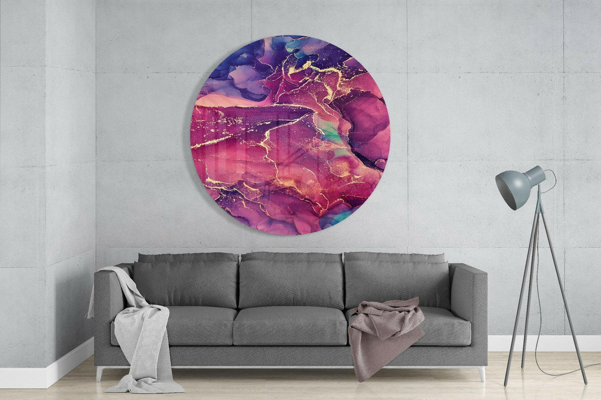 Magenta purple gold ink round glass wall art above a gray sofa beside a tripod floor lamp on a pale concrete wall