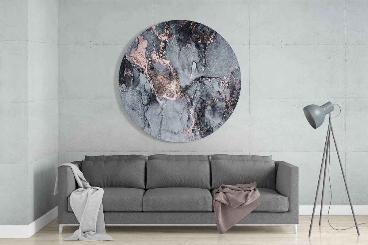 Slate gray and copper marble round glass wall art above a gray sofa beside a gray tripod floor lamp on a pale concrete wall