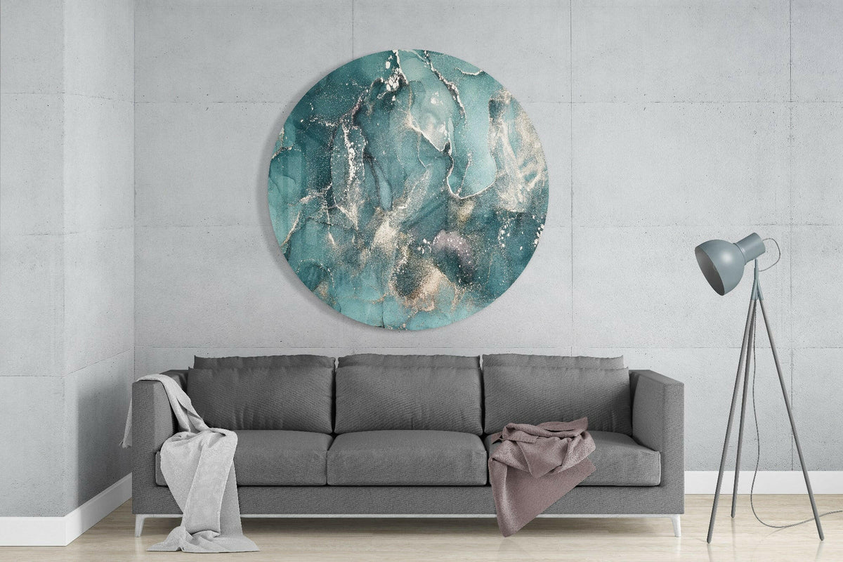 Teal green and gold marble round glass wall art above a gray sofa beside a gray tripod floor lamp on a pale concrete wall