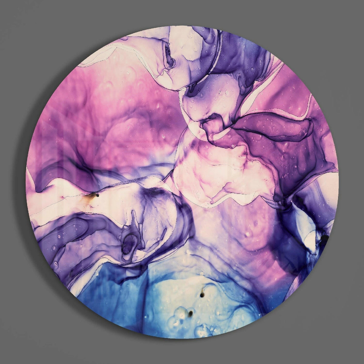 Pink and blue fluid marble round glass wall art hanging on a plain gray wall