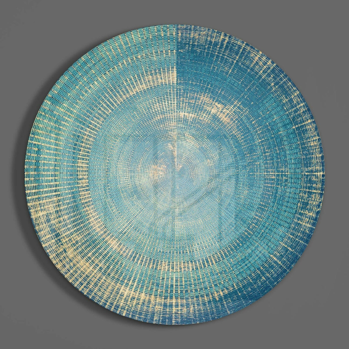 Teal concentric rings abstract round glass wall art hanging on a plain gray wall