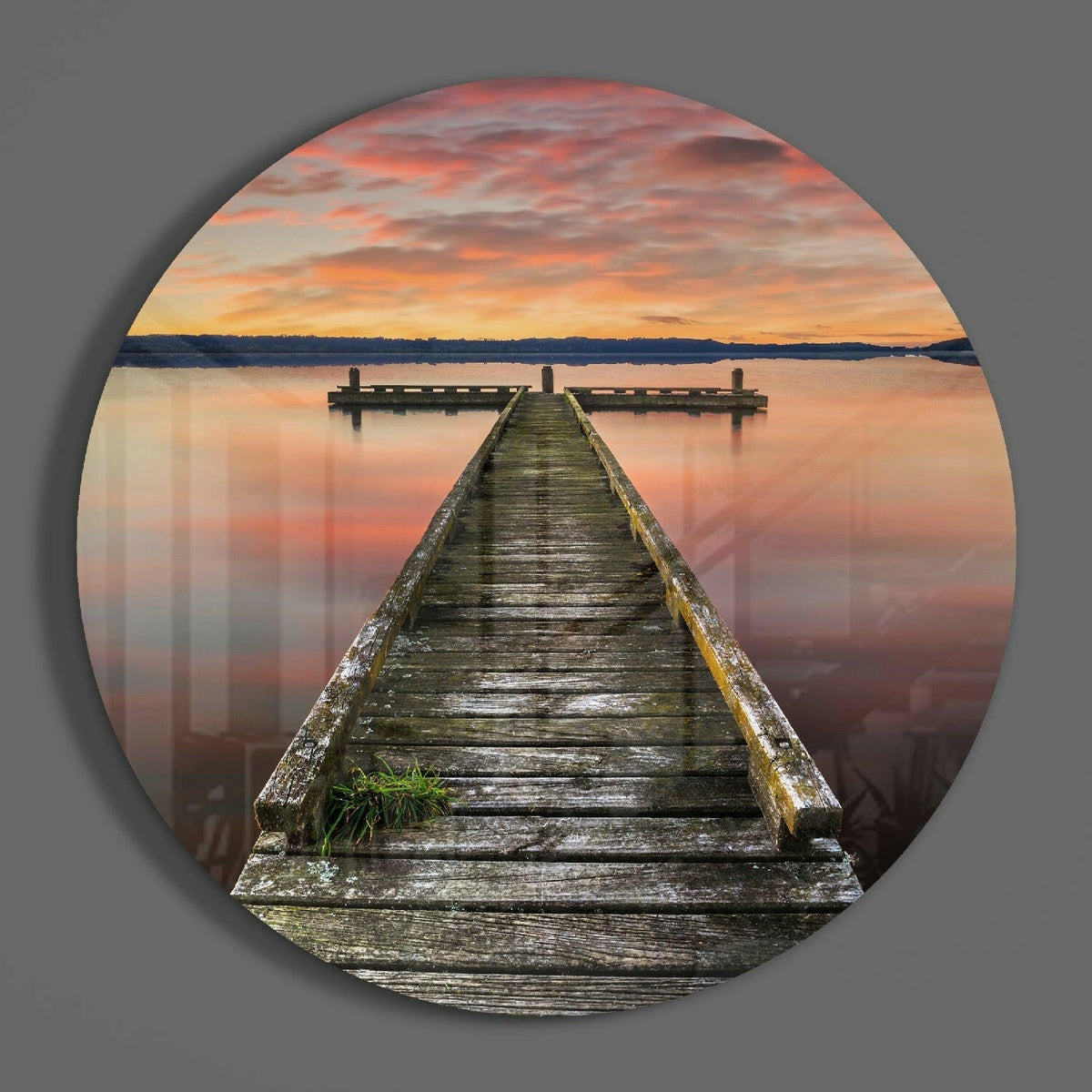 Wooden jetty at dawn round glass wall art hanging on a plain gray wall