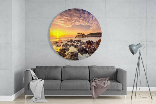 Pier at sunrise round glass wall art above a gray sofa beside a tripod lamp