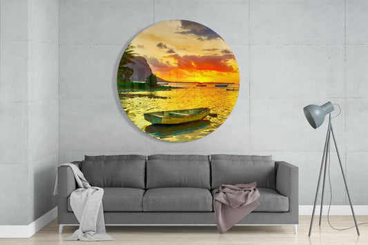 Boat on a golden sunset lagoon round glass wall art above a gray sofa beside a tripod floor lamp on a pale concrete wall