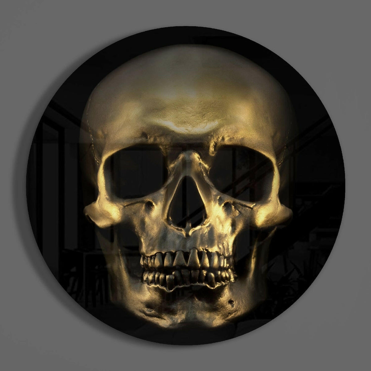 Gold skull round glass wall art on a plain gray wall, glossy glass disc seen from the front