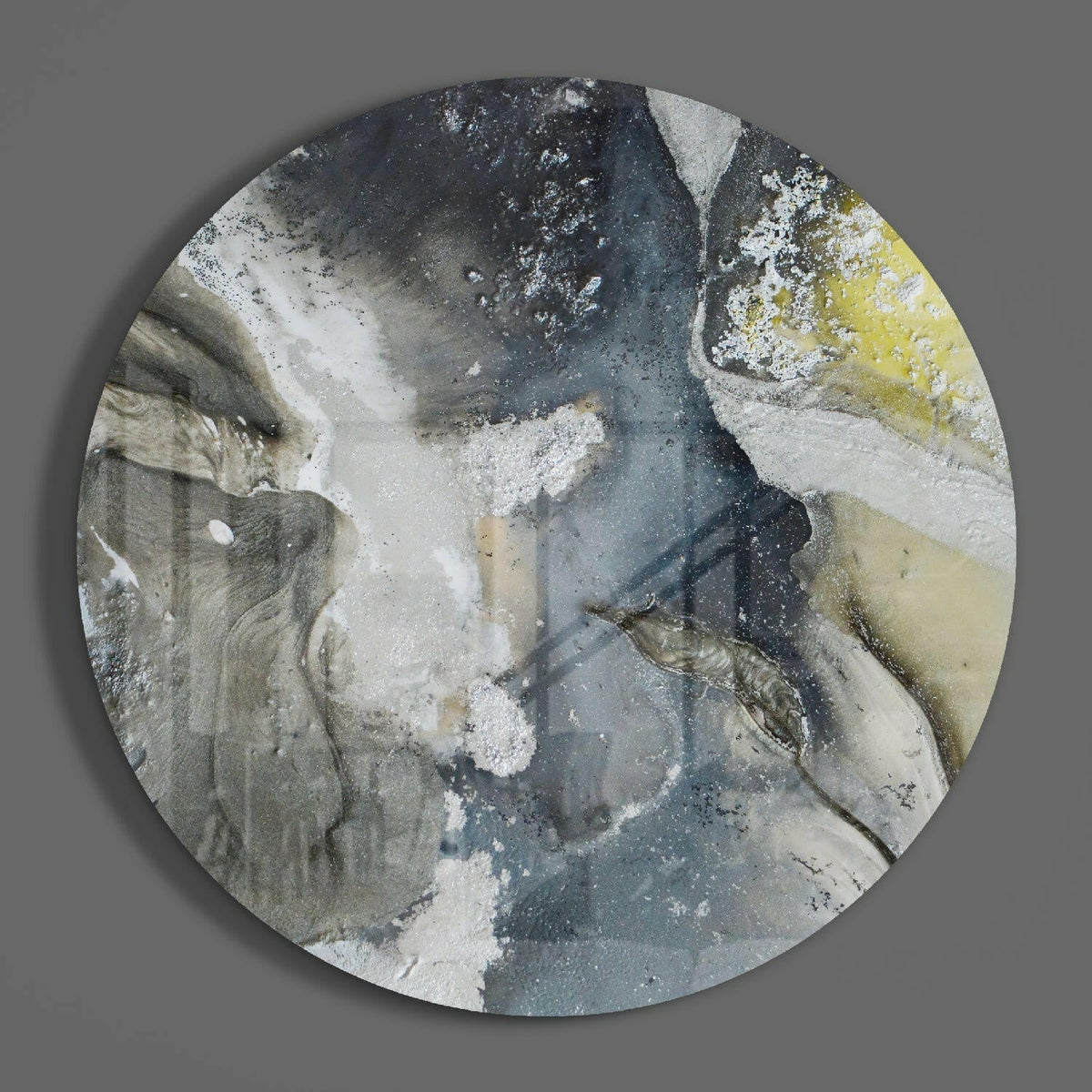 Gray and yellow marble round glass wall art on a plain gray wall, glossy glass disc seen from the front