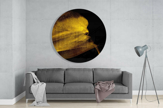 Golden shimmer sweep round glass wall art above a gray sofa beside a tripod floor lamp on a pale concrete wall