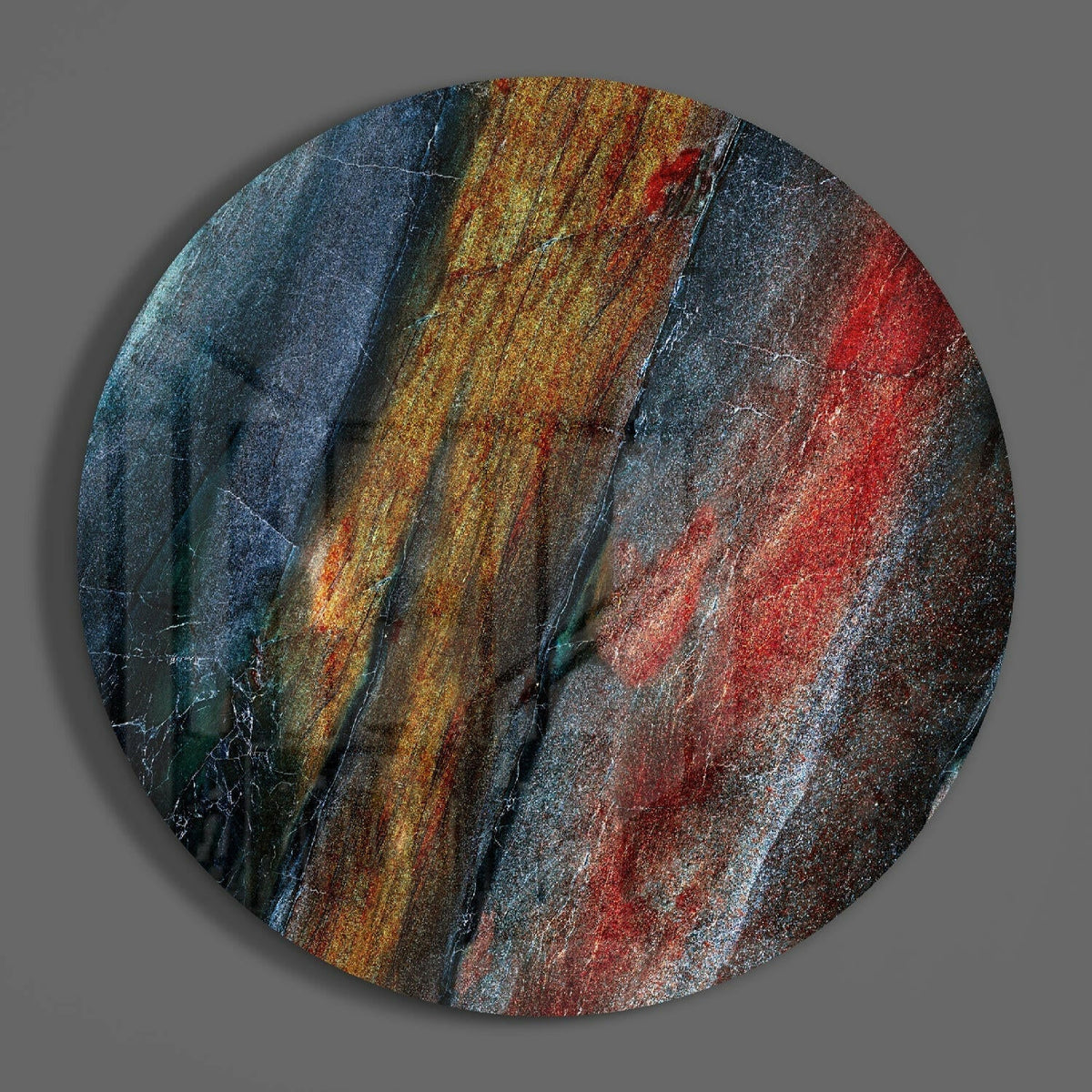 Red and blue mineral stone round glass disc casting a soft shadow on a gray wall