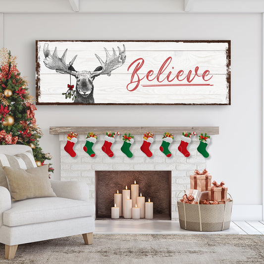 Believe Christmas moose canvas sign above a white brick fireplace hung with red and green stockings