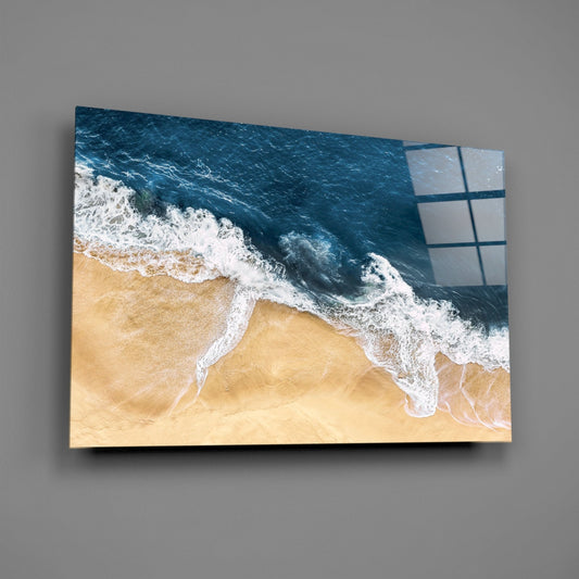 Navy surf on tan sand glass wall art on a gray wall, light reflecting off the glossy front