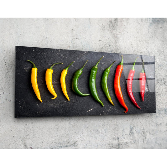 Chili peppers on black slate panoramic glass wall art on a pale concrete wall, angled to show the glossy surface