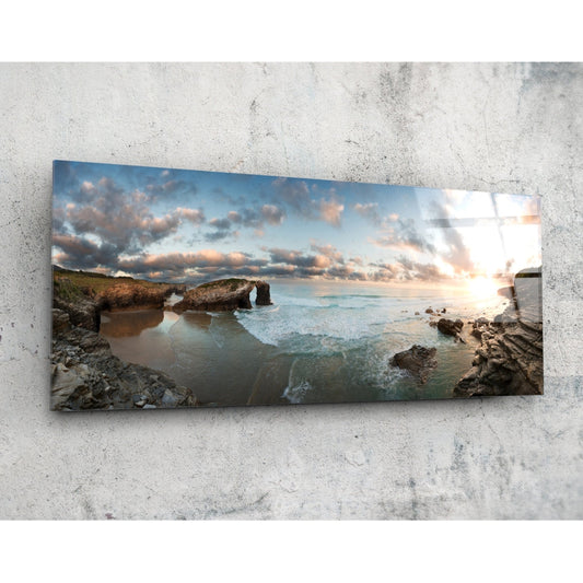 Rock arch coastline at sunset glass wall art on a pale concrete wall