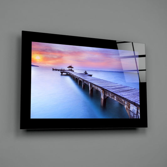 Long pier to a gazebo at lavender sunset glass wall art with a black border hung on a plain gray wall