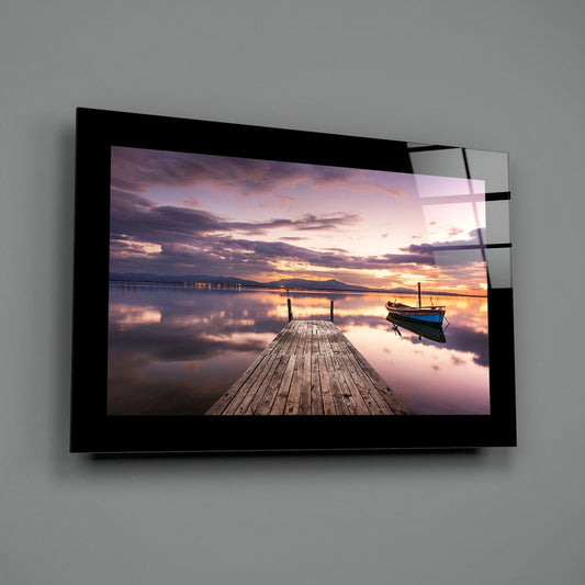 Wooden pier and moored boat at purple dusk glass wall art with a black border hung on a plain gray wall