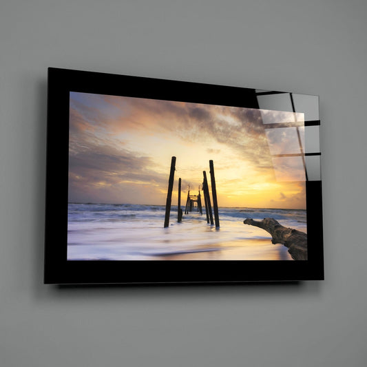 Old pier pilings in golden sunset surf glass wall art with a black border hung on a plain gray wall
