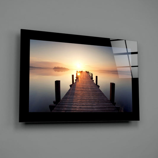 Wooden jetty on a misty lake at golden sunrise glass wall art with a black border hung on a plain gray wall