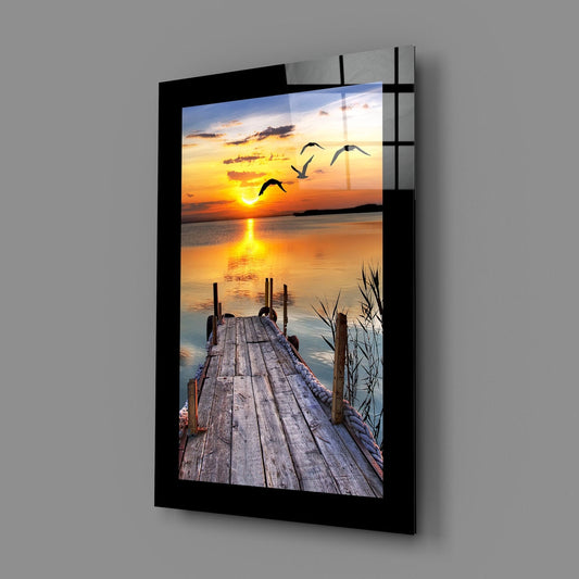 Wooden pier at sunset with birds glass wall art on a plain gray wall