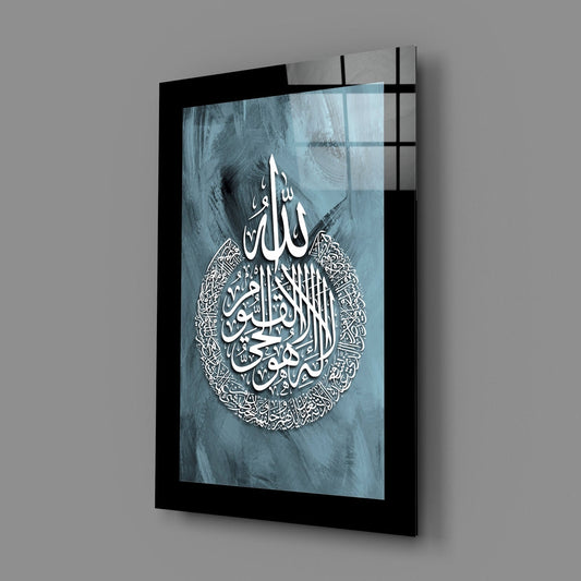 Black border teal Ayatul Kursi calligraphy glass wall art hanging on a plain gray wall, seen at an angle