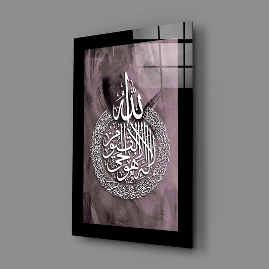 Black border mauve Ayatul Kursi calligraphy glass wall art hanging on a plain gray wall, seen at an angle