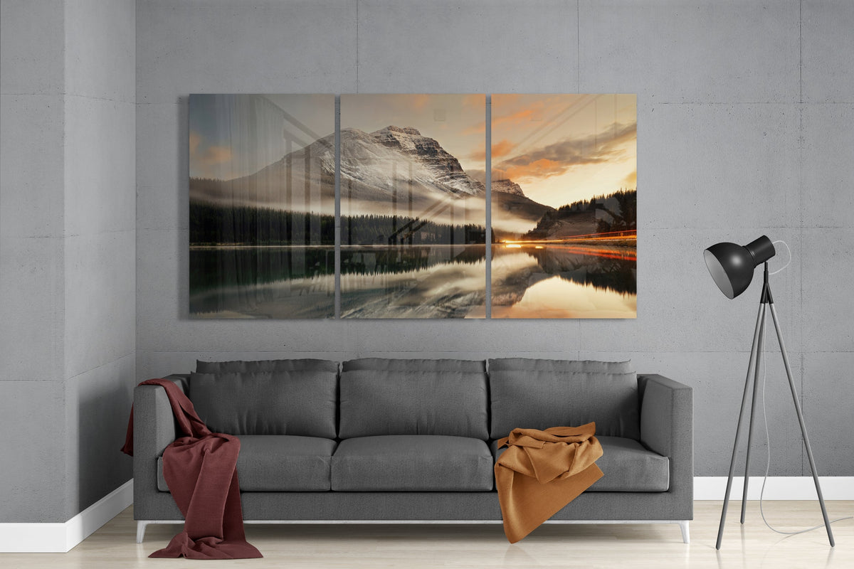 Snowy mountain lake 3-panel glass wall art set above a gray sofa beside a black floor lamp