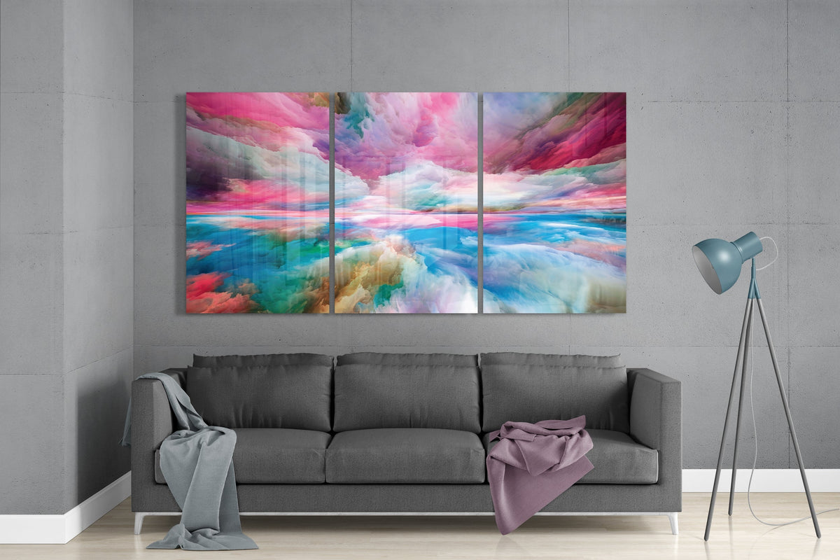 Pink and teal dreamy cloudscape glass wall art set above a gray sofa beside a tripod floor lamp