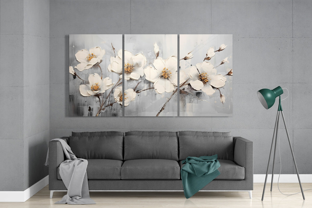 White blossom branches 3-panel glass wall art set above a gray sofa beside a green tripod floor lamp