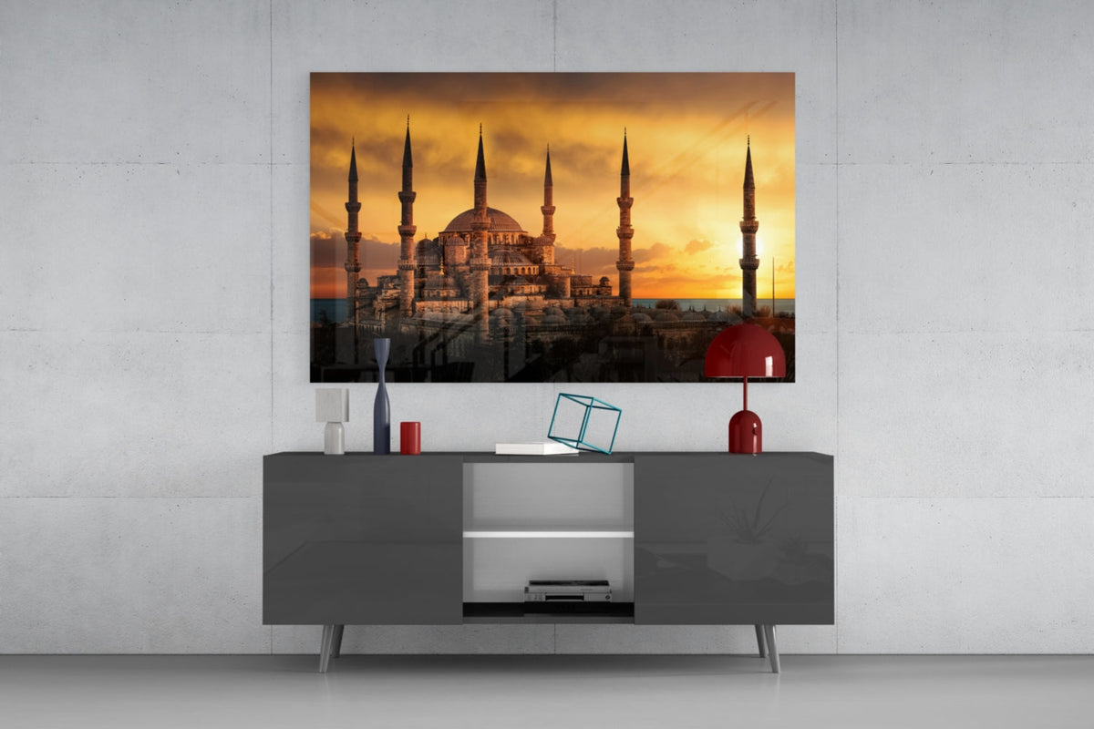 Mosque at golden sunset glass wall art above a gray sideboard with a red table lamp