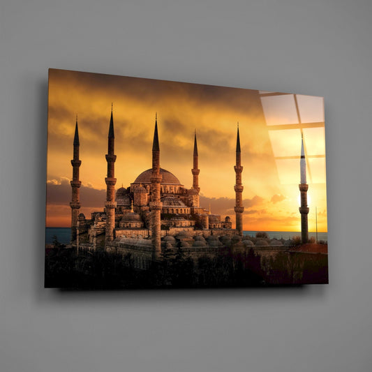 Mosque at golden sunset glass wall art hanging on a plain gray wall, seen at an angle