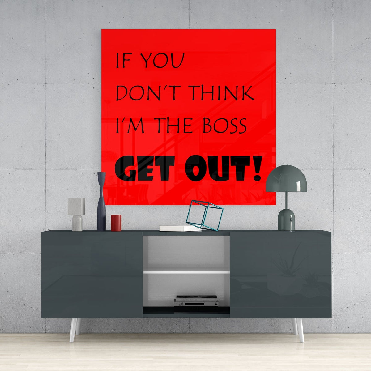 Funny boss quote in black text on red square glass wall art above a dark gray sideboard with a gray table lamp