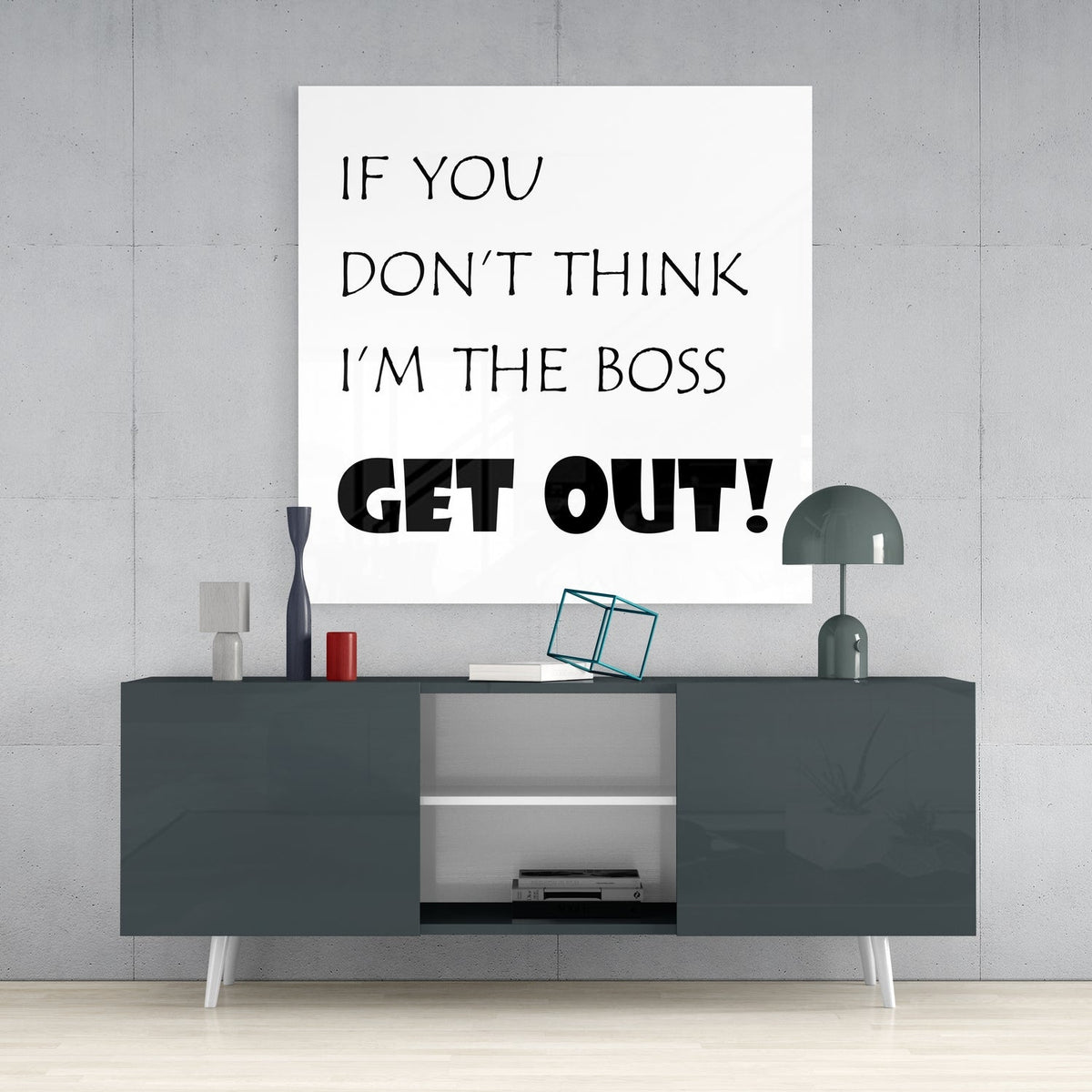Funny boss quote in black text on white square glass wall art above a dark gray sideboard with a gray table lamp