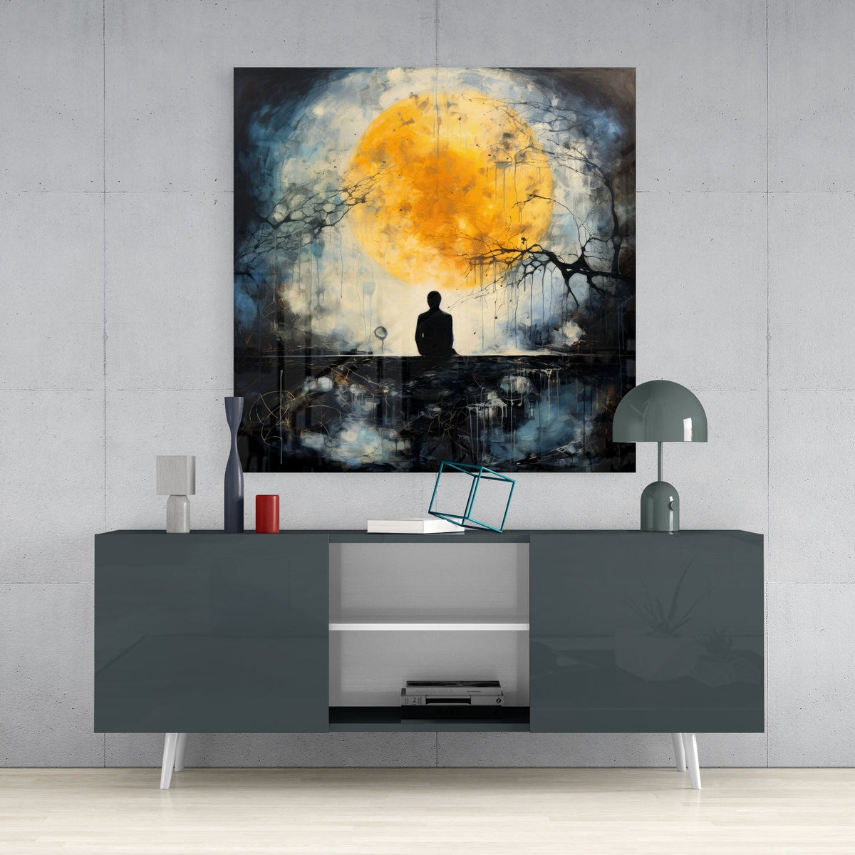 Golden full moon and lone figure glass wall art above a gray sideboard with a vase, red candle and dome lamp