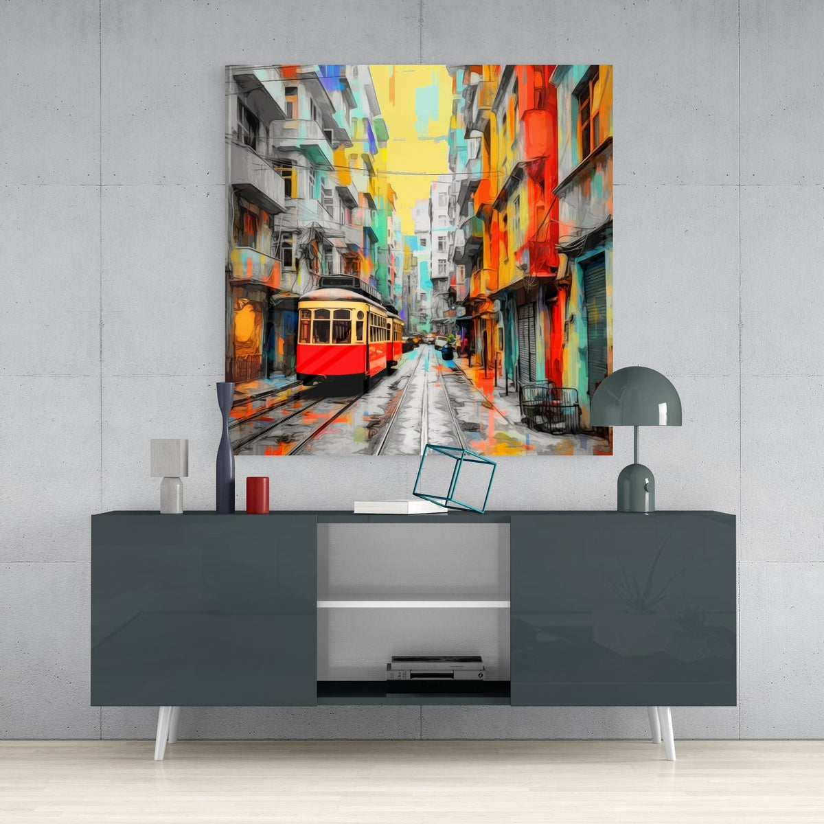 Red tram on a colorful street glass wall art above a gray sideboard with a small lamp